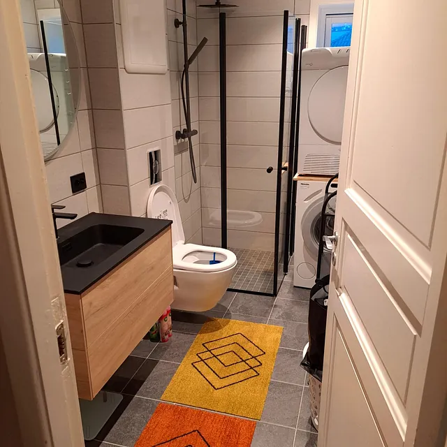 Moderne bad med dusjkabinett, vaskemaskin og varmefarget gulvteppe.