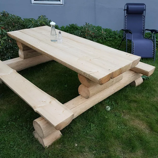 Solid piknikbord av tømmer med vannflaske og saltbøsse, samt en lenestol i bakgrunnen.