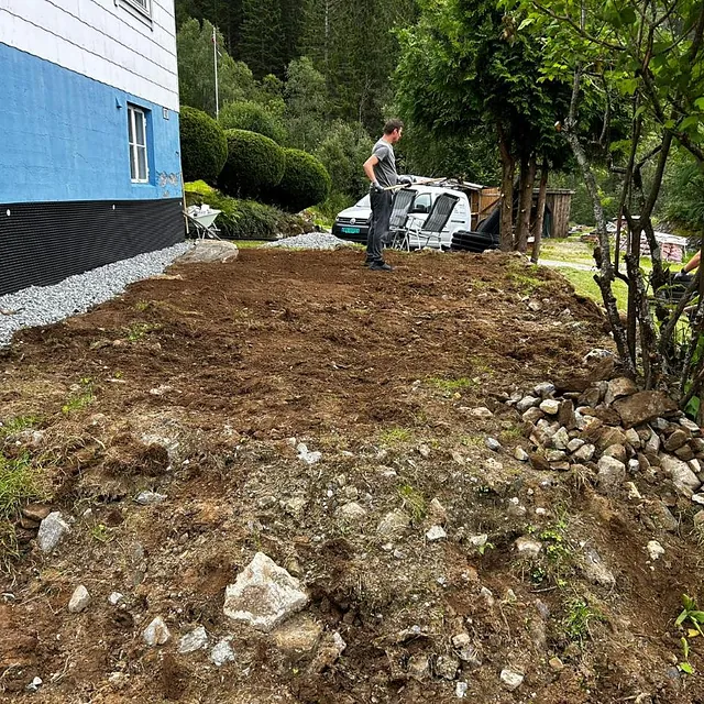Arbeid med planering av jord ved et hus, personer og arbeidsutstyr på stedet.