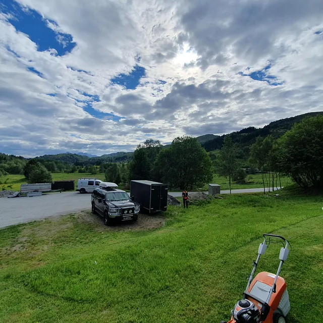 Parkeringsplass med gressplen, noen biler og utsikt til dal og fjell.