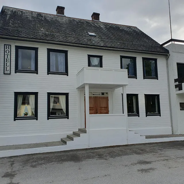 Hvitt to-etasjes hotellbygg med skilt og inngangsparti i tre.