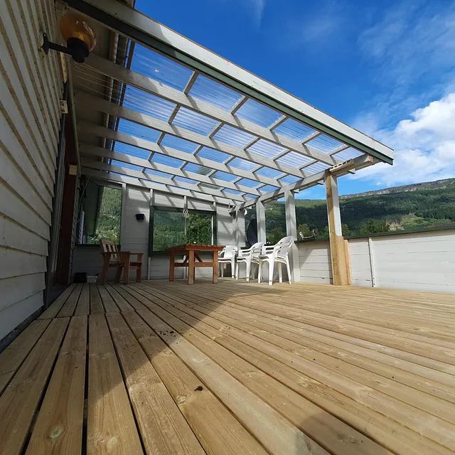 Romslig terrasse med tak og sitteplasser, utsikt til grønt landskap og blå himmel.